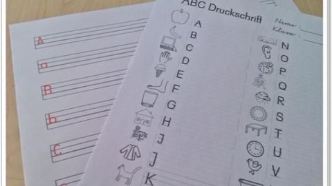Zwei Übungsblätter liegen nebeneinander auf einem Tisch, das eine mit Linien zum Schreiben, das andere mit Buchstaben und Bildern.