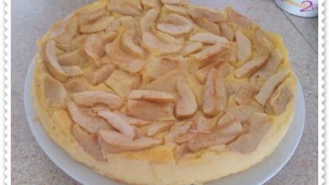 Ein Grießkuchen mit Äpfeln auf weißem Teller; die Apfelscheiben sind ordentlich auf dem Kuchen verteilt.
