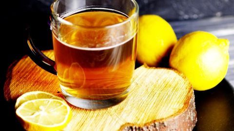 Ein Glas Tee steht auf einem Holzbrett, umgeben von frischen Zitronen, die für zusätzlichen Geschmack sorgen.
