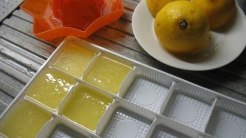 Einfrierformen mit frischem Zitronensaft sind auf einem Tisch platziert, während mehrere ganze Zitronen in der Nähe liegen.
