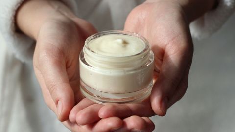 Eine Hand hält ein Glas mit selbstgemachtem Deo ohne Aluminium, umgeben von einem weichen, weißen Hintergrund.