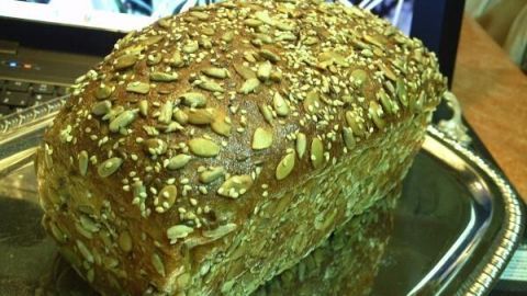 Ein Laib Eiweißbrot liegt auf einem silbernen Tablett, mit vielen Körnern bedeckt; im Hintergrund ein Laptop-Bildschirm. Text: "2012/09/06".