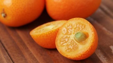 Kumquat-Hälften liegen auf Holztisch, leuchtend orange, eine ist aufgeschnitten und zeigt saftiges Fruchtfleisch.