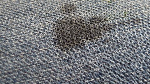 Ein Schmierfleck ist auf einer blauen Jeans sichtbar, der durch einen unachtsamen Kontakt entsteht, wodurch der Stoff beschädigt wird.