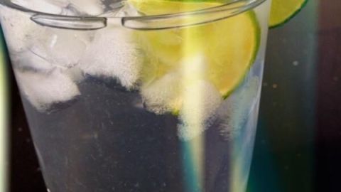 Ein Glas mit Limettenwasser und Eiswürfeln steht auf einem Tisch. Eine Limettenscheibe ziert den Glasrand.