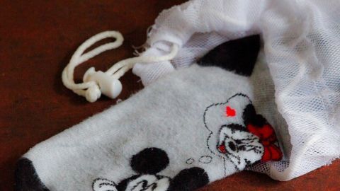 Eine bunte Socke mit Mickey-Maus-Motiv steckt aus einem Wäschebeutel auf einem Holztisch. Der Beutel ist weiß und geschlossen.