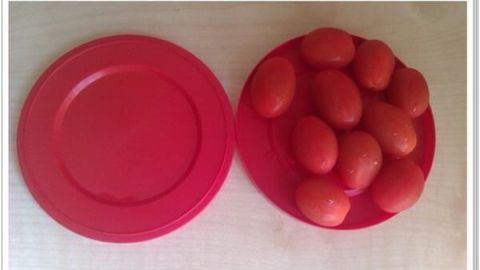Cherrytomaten liegen auf einem roten Teller, bereit zum Halbieren, auf einem hellen Holztisch für einfaches Schneiden.