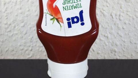Eine Ketchupflasche steht aufrecht auf einem Tisch und scheint bereit zum Ausgießen des Tomatenketchups.
