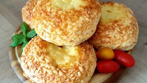 Käsebrötchen liegen golden braun auf einem Holzbrett, umgeben von bunten Tomaten und frischem Basilikum.