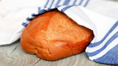Ein frisches Brot liegt auf einem Holzbrett, teilweise in ein gestreiftes Tuch eingewickelt, bereit zum Servieren.