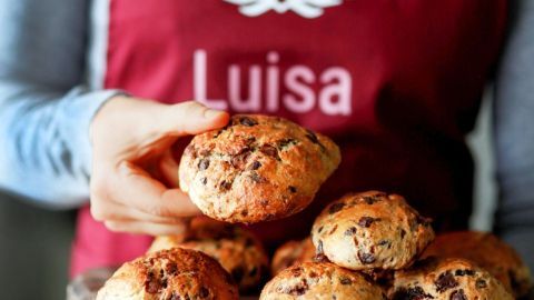 Frisch gebackene Schokobrötchen werden von einer Person auf einem Holzbrett präsentiert, umgeben von einem gemütlichen Küchenambiente.