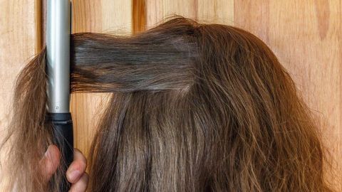 Eine Person hält ein Lockengerät, während sie ihre Haare frisiert, um mögliche Nissen zu entfernen.