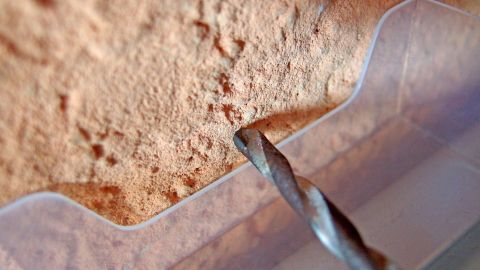 Ein Bohrer bohrt in eine Wand, während ein Staubschutzbehälter ihn umgibt, um Staub auf dem Boden zu vermeiden.