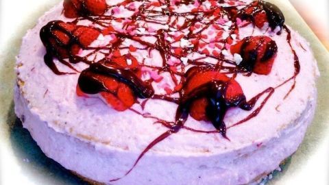Eine Erdbeer-Joghurt-Torte mit roter Fruchtsauce und frischen Erdbeeren, platziert auf einem hellen Teller.
