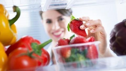Frische Erdbeeren werden aus einem Behälter im Kühlschrank genommen, um gesunde Snacks vorzubereiten.