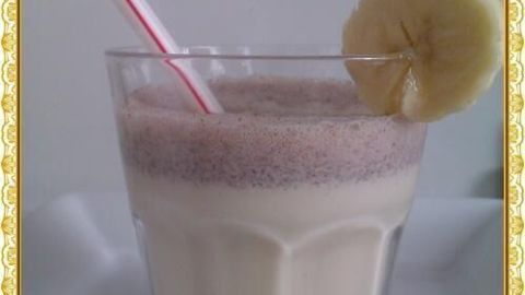 Ein Glas Milchshake mit Bananenscheibe und rot-weißem Strohhalm steht auf einem weißen Teller.