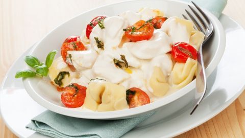 Eine Schüssel Sahnesoße umhüllt gefüllte Teigtaschen und Tomaten, in einem hellen Holzrahmen arrangiert.