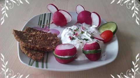 Radieschen und ein cremiger Aufstrich sind auf einem Teller arrangiert, umgeben von Vollkornbrot und frischem Gemüse.