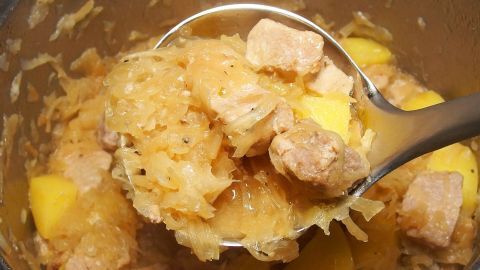 Ein Löffel mit einer Mischung aus Sauerkraut, Kasslerkotlett und Kartoffeln wird aus einem Topf gehoben.