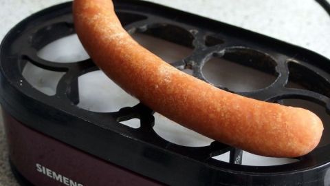 Schnell, einfach und besonders lecker, kann man Würstchen im Eierkocher zubereiten. Ein Würstchen liegt auf einem Eierkocher, während es erhitzt wird. Der Küchenuntergrund ist hell und modern.
