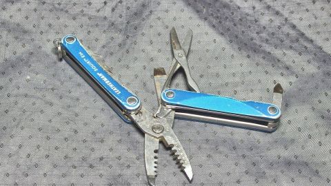 Ein multifunktionales Taschenwerkzeug liegt offen auf einem grau gepunkteten Untergrund und zeigt seine verschiedenen Einsatzmöglichkeiten.
