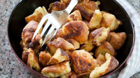 In einer schwarzen Schüssel liegt herzhaft gebratener Kaiserschmarren, während eine Gabel ihn auflockert. Der Untergrund ist eine graue, gemusterte Arbeitsplatte.