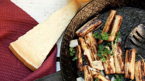Gebratener Spargel liegt in einer Pfanne, überzogen mit Honig und Parmesankäse, umgeben von frischen Kräutern.