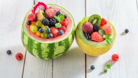 Ein halbierter Wassermelone mit buntem Obstsalat gefüllt, auf einem hellen Holztisch dekoriert.