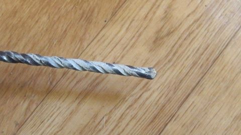 Ein Bohrer liegt auf einem Holzboden. Er wirkt abgenutzt und könnte für das Entfernen von Angebranntem in Töpfen verwendet werden.