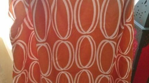 Orangene Kinderschürze mit weißem Kreis-Muster hängt an einem Kleiderbügel im Sonnenlicht, in einem Zimmer.