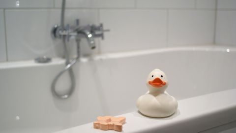 Eine Gummi-Ente sitzt auf der Badewannenkante, während ein Wasserhahn funktioniert und eine ruhige Badezimmerumgebung bietet.