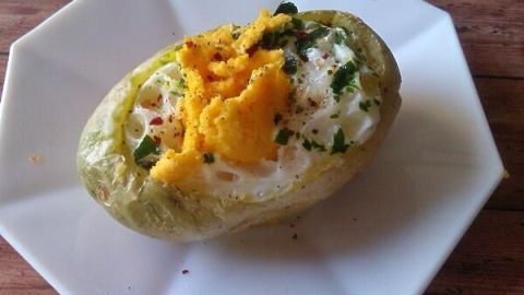 Eine gefüllte Kartoffel mit Rührei und frischen Kräutern liegt auf einem weißen Teller und sieht appetitlich aus.