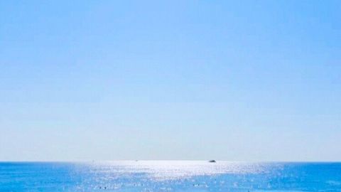 Strandliegen mit Sonnenschirmen stehen am Sandstrand, während die Sonne über dem glitzernden Wasser strahlt.