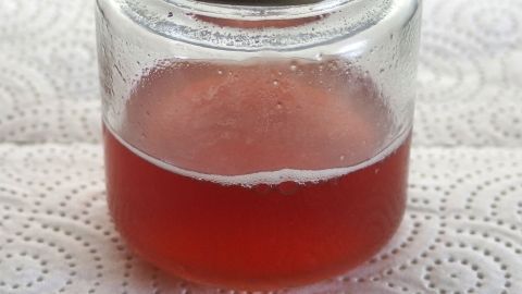 Ein Marmeladeglas mit einer roten Flüssigkeit darin wird einfach ausgespült und steht auf einem Küchentuch.