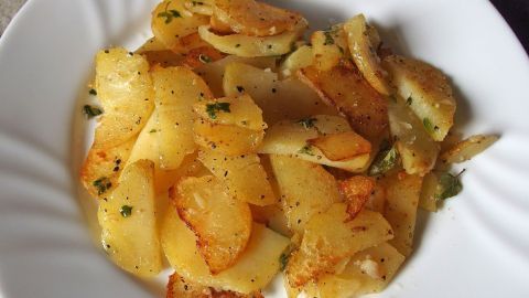 Goldbraune Knoblauchkartoffeln liegen appetitlich auf einem weißen Teller, umgeben von frischen Kräutern.