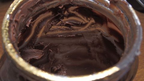 Ein fast leerer Nutella-Glas mit restlicher Schokolade, steht auf einem Tisch, umgeben von einem häuslichen Umfeld.