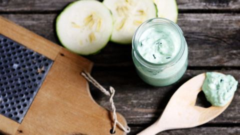 Zucchini-Scheiben liegen neben einem Glas mit Mascarpone-Soße und einer Reibe auf einer rustikalen Holzoberfläche.