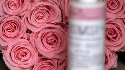 Eine Flasche Hautpflegeprodukt steht im Vordergrund, während sie von einer rosa Rosenblüte umgeben ist, die ein pflegendes Ambiente schafft.