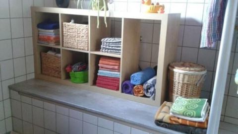 Badewannenregal organisiert bunte Handtücher und Pflanzen auf weiß gefliesten Wänden, nutzloser Raum kreativ genutzt.