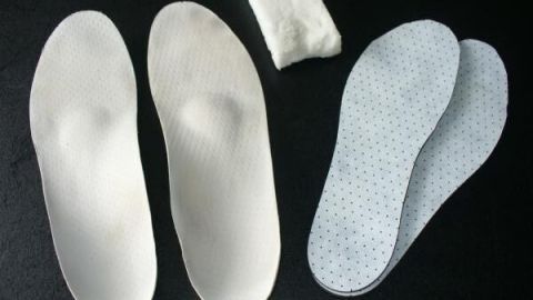 Orthopädische Schuheinlagen liegen neben einem Reinigungstuch auf einer dunklen Oberfläche und sind bereit zur Pflege.