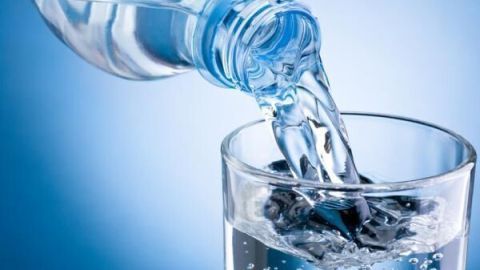 Wasser wird aus einer Plastikflasche in ein klares Glas gegossen, umgeben von einem blauen Hintergrund.