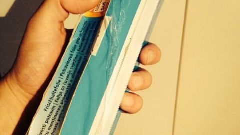Eine Hand hält eine Rolle Frischhaltefolie in einem hellen Raum, bereit zum Abreißen für die Verwendung.