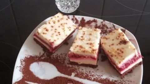 Eine elegante Karamell-Mascarpone-Himbeerkuchen-Präsentation auf einem Teller, umgeben von Kakaopulver und frischen Blumen.