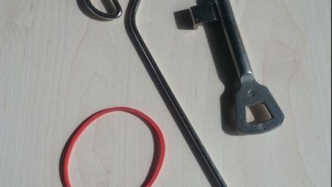 Ein Zimmerschlüssel liegt neben einem Schlüsselring und einem gummierten Band auf einer hellen Oberfläche, bereit zur Sicherung.
