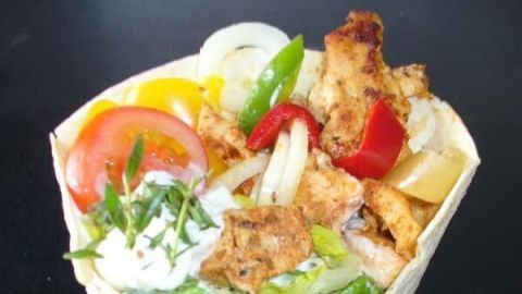 Ein gefüllter Wrap mit Hähnchen, frischem Gemüse und Soße wird in einer weißen Schale präsentiert.