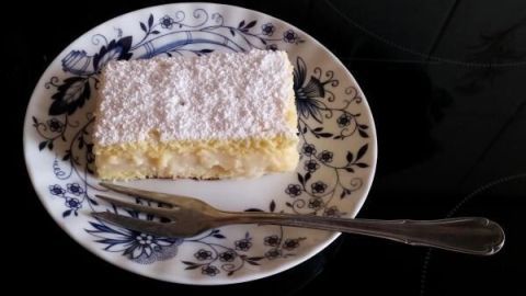 Ein Stück Zitronencremekuchen liegt auf einem blauen Teller mit Blumenmuster, dekoriert mit Puderzucker, neben einer Gabel.