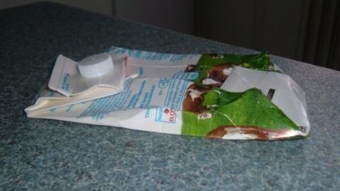 Ein zusammengefalteter Verpackungskarton liegt auf einer Arbeitsfläche. Er wird vorbereitet, um im gelben Sack Platz zu sparen.