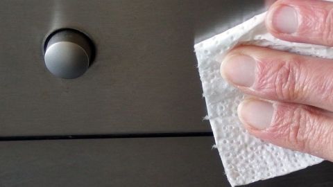 Eine Hand wischt mit einem Tuch über ein Edelstahlgerät, um es streifenfrei zu reinigen.