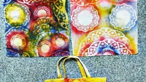 Bunte Taschen mit Mandala-Mustern liegen auf grauem Boden; kreativ verzierte Beutel in kräftigen Farben.
