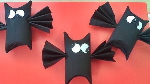 Papierfledermäuse liegen dekorativ auf einem roten Hintergrund, kreativ mit Kindern gebastelt, zeigen große, neugierige Augen.